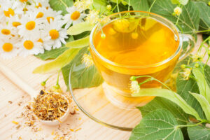 a cup of linden and chamomile tea with the corresponding plant material next to the glass tea cup