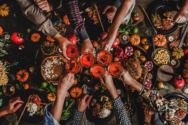 friends holding wine glasses over fall feast table, filled with food